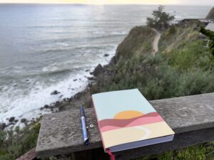 journal and pen resting on a railing overlooking the ocean